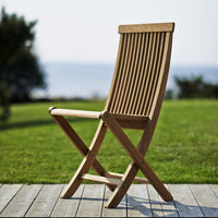 "Natural wood finish chair with slatted design, set against a green lawn and blue ocean backdrop."