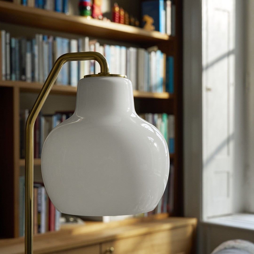 White lamp with gold arm on a wooden surface in front of a bookshelf