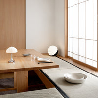 Minimalist dining room with wood tones, soft beige textiles, and a light gray circular bowl. Clean, modern aesthetic.