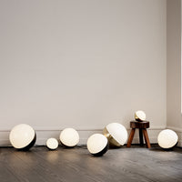 White and gold spherical lamps with a sleek black base, arranged on a wooden floor against a neutral wall.
