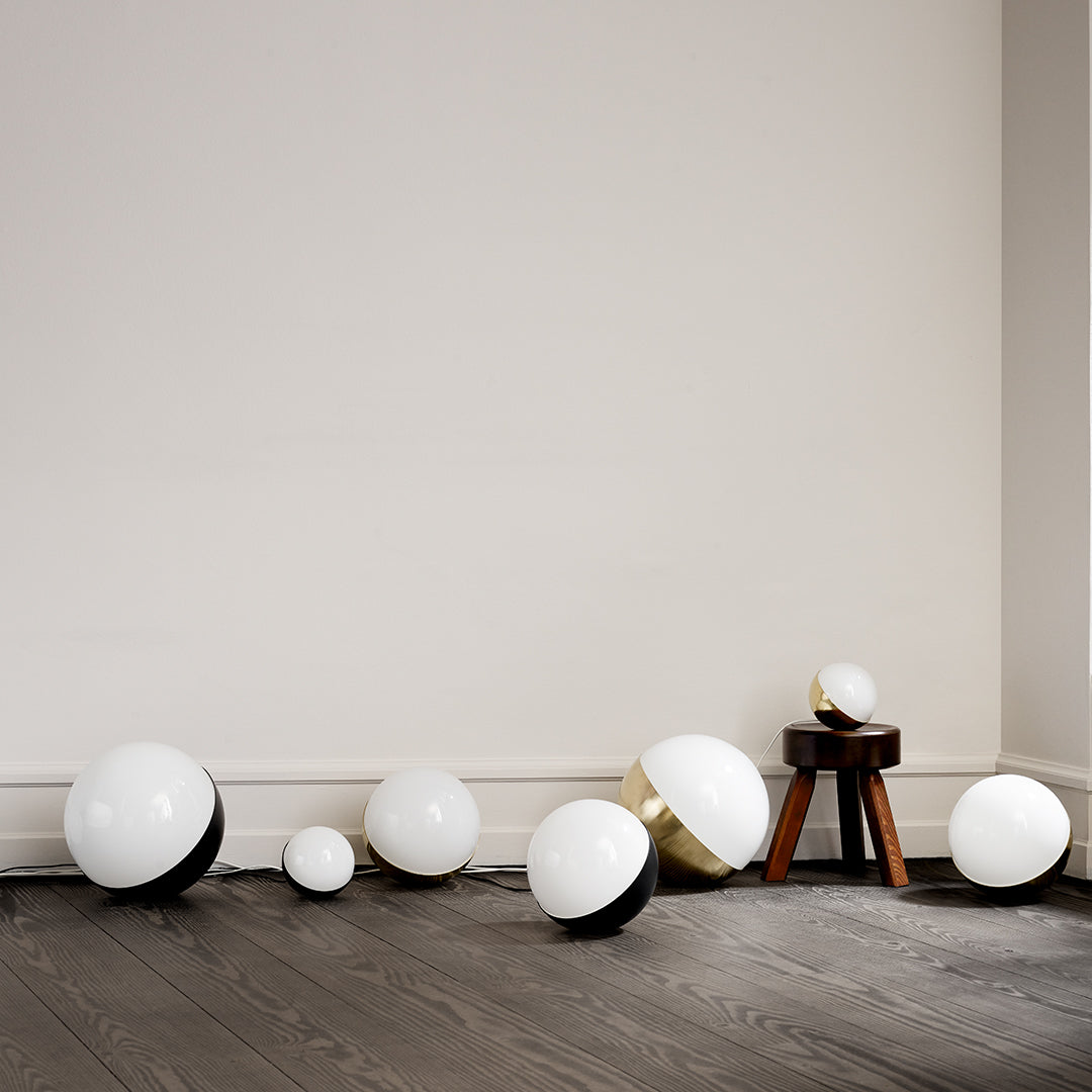 Glossy white and black spherical decor elements with gold accents on a wooden floor against a neutral wall.
