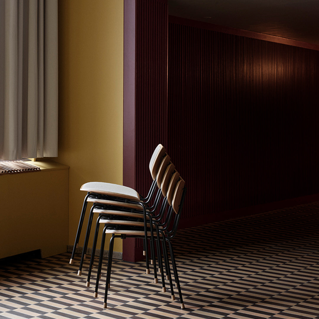 Stacked chairs with black metal legs, light beige seats, against a backdrop of deep burgundy walls and geometric patterned flooring.