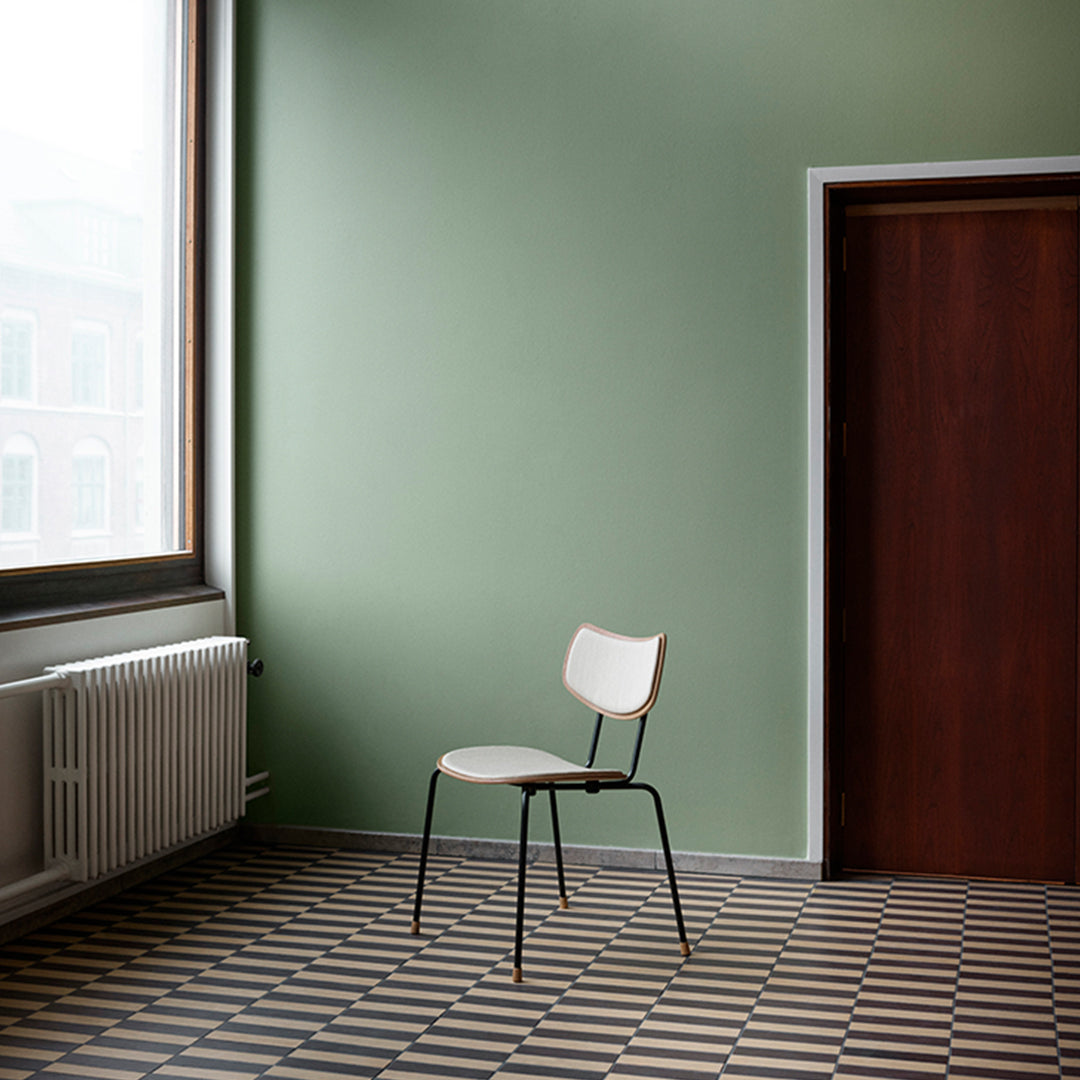 Minimalist white chair with black legs in a room featuring green walls and a geometric patterned floor in black and beige.