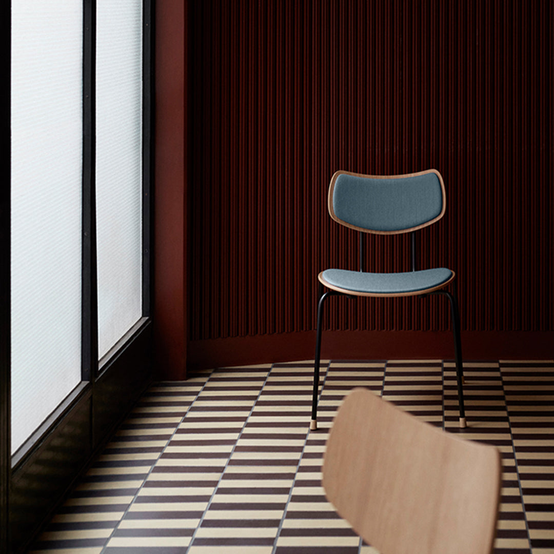 Light blue chair on a black-and-white checkered floor against a dark red wall with vertical lines.