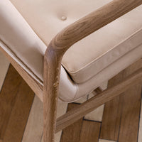 Beige cushioned chair with natural wood frame and subtle button detail, set against a patterned wooden floor.