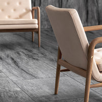Beige upholstered armchair with wooden frame on textured gray flooring. Elegant and modern design.