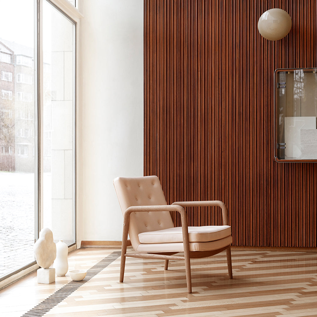 Beige armchair with tufted upholstery against a wooden wall, featuring a striped light and dark wood floor.