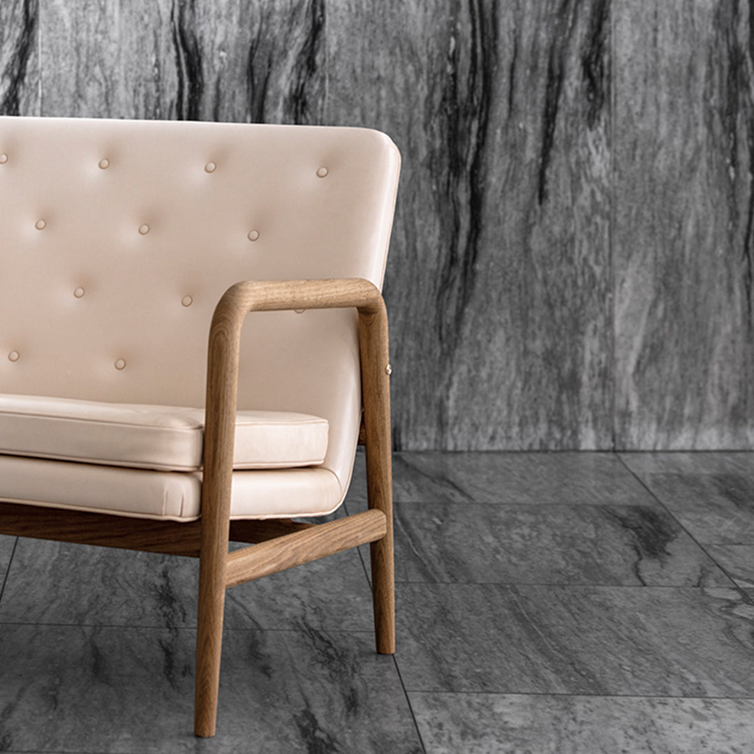 Blush pink tufted sofa with natural wood frame against a textured gray backdrop. Modern minimalist design elements.