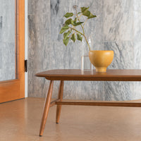 Wooden coffee table with a warm brown finish, paired with a vibrant yellow bowl against gray marble wall.