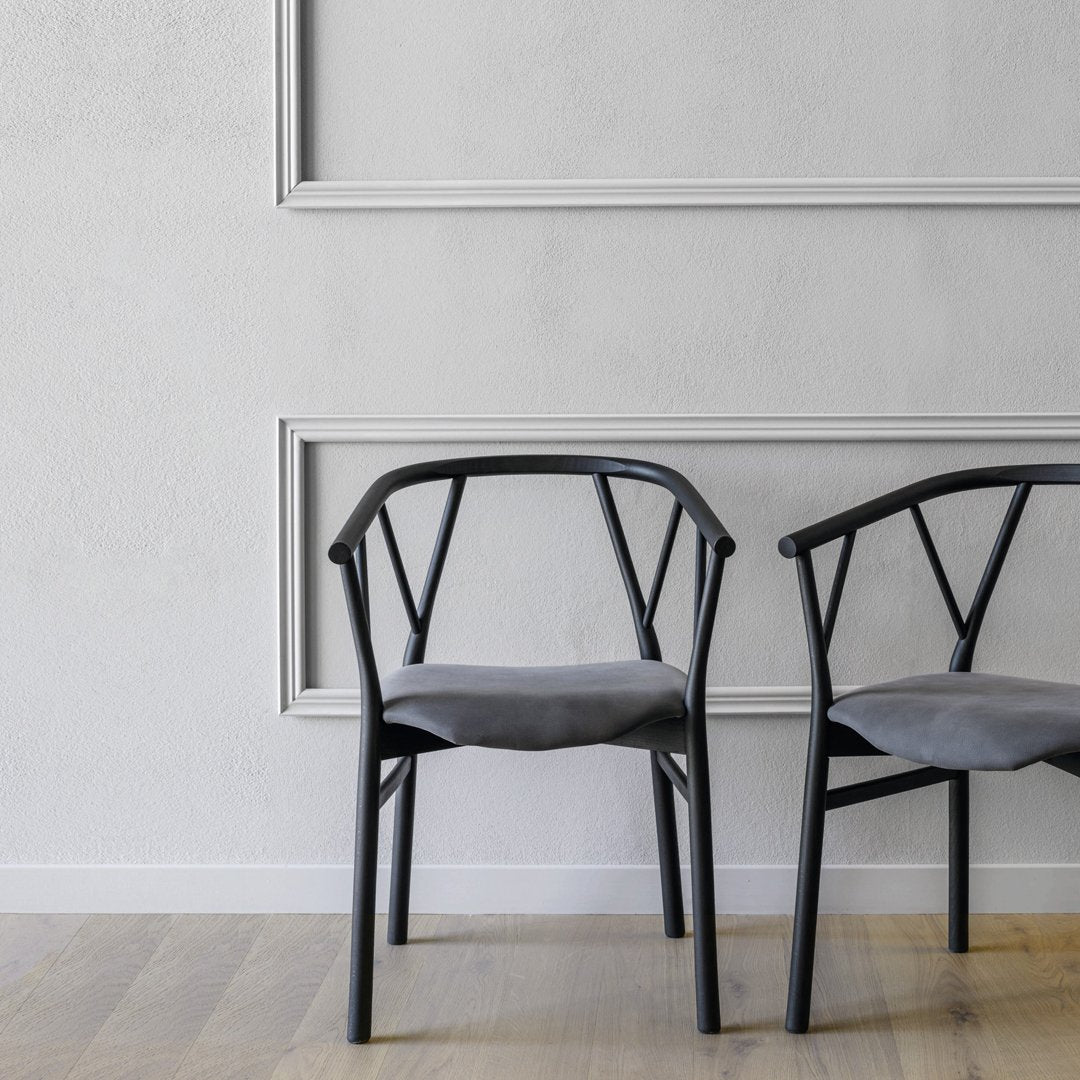 "Modern black chairs with grey cushions against a neutral wall, featuring minimalist design and subtle patterns."