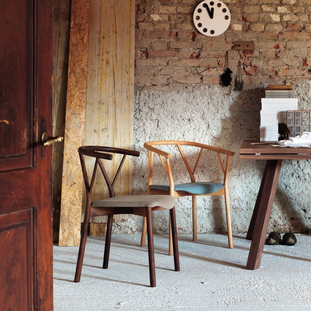 Wooden chairs with natural and dark finishes, set against a textured brick wall and minimalist decor.