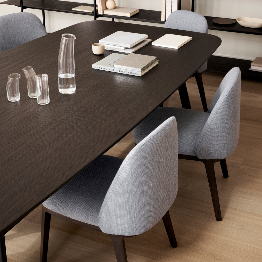 "Modern dining table with a dark wood finish, paired with light gray upholstered chairs in a minimalistic pattern."