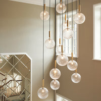 Cluster of clear glass pendant lights with textured patterns and gold accents, hanging against a neutral wall.
