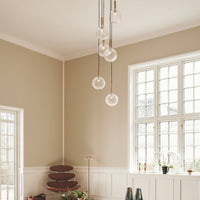 Modern pendant lights with clear glass shades, set against a neutral beige wall and a muted brown shelf.