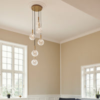 Elegant pendant light with clear globe bulbs and a sleek, brass finish, set against a neutral wall and bright windows.