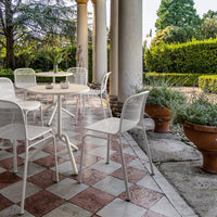 White outdoor chairs surrounding a round table on a tiled floor with red and white checkerboard pattern.