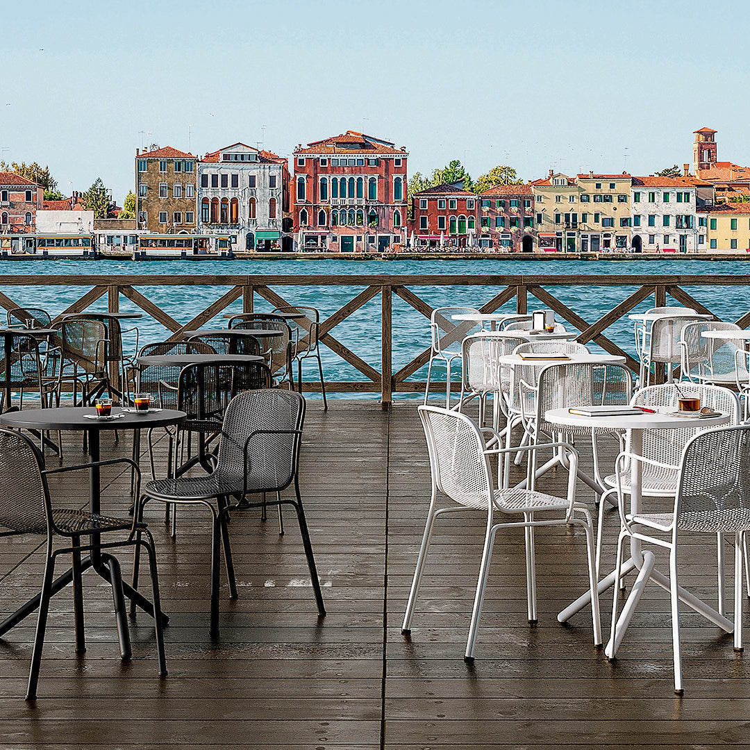 Outdoor dining set featuring black and white chairs on a wooden deck with a vibrant waterfront backdrop.