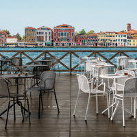 Outdoor dining set featuring black and white chairs on a wooden deck with a vibrant waterfront backdrop.
