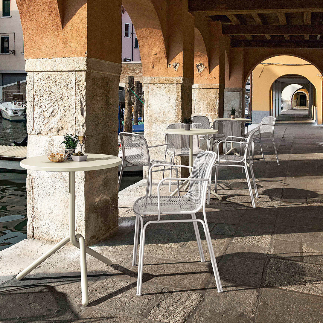 White metal chairs and tables against warm stone and vibrant archway colors, creating a stylish outdoor dining scene.