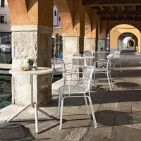White metal chairs and tables against warm stone and vibrant archway colors, creating a stylish outdoor dining scene.