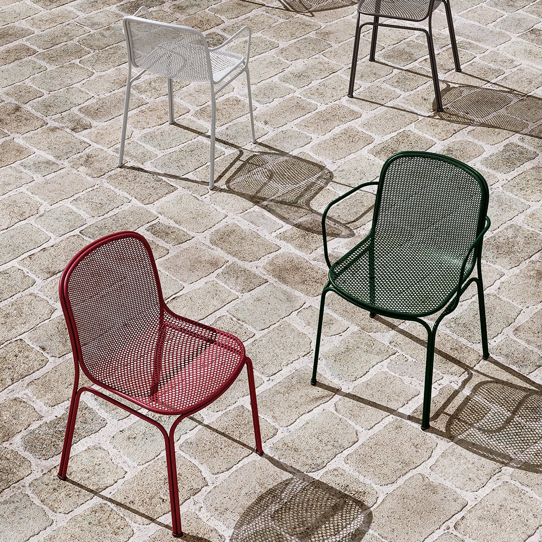 Colorful metal chairs in red, green, and white set against a textured stone floor, showcasing modern design and patterns.