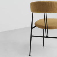 Round chair with textured mustard fabric upholstery and sleek black metal legs, set against a light gray background.