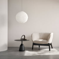Stylish cream-colored chair with a textured pattern, black accent table, and a minimalist white paper pendant lamp.