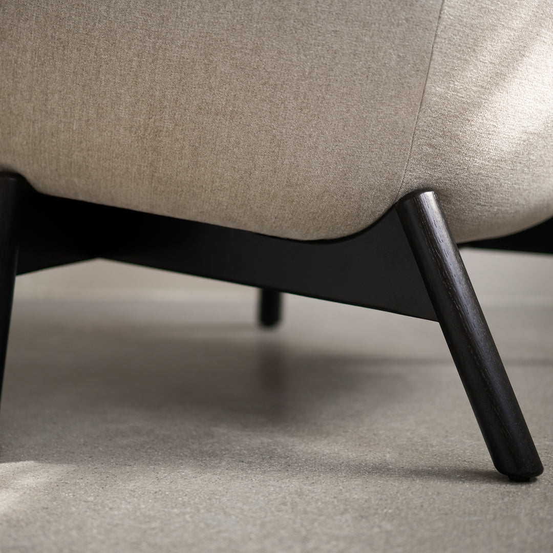 Beige upholstered sofa with a smooth texture and sleek black wooden legs, offering a modern and minimalist design.