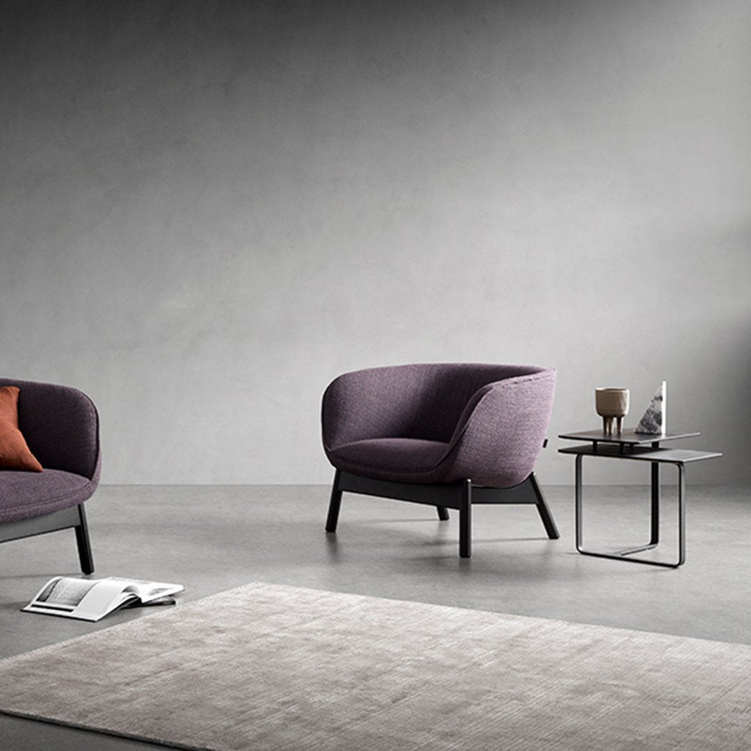 "Purple upholstered chairs with solid black legs and a light gray textured rug in a modern, minimalistic setting."