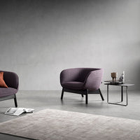 "Purple upholstered chairs with solid black legs and a light gray textured rug in a modern, minimalistic setting."