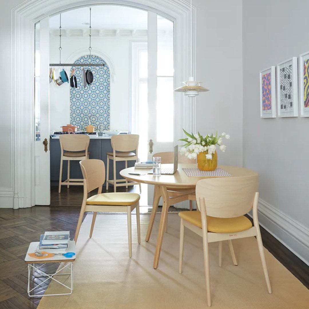 Light wood dining table with yellow and beige chairs, accented by blue patterned wall decor and neutral tones.