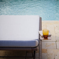 Light gray cushion on a poolside lounge chair with a textured surface, complemented by a vibrant yellow-orange drink.