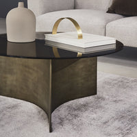 "Modern round coffee table with a sleek black glass top and bronze sculptural base, surrounded by a soft, neutral rug."