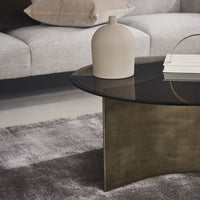 Stylish black glass coffee table with a sleek brass base, paired with a neutral-toned vase and textured gray rug.