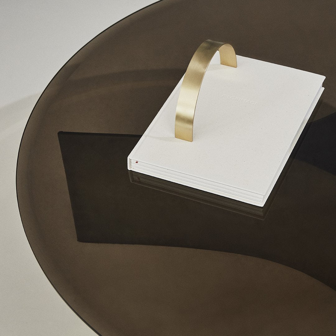 White notebook with gold handle on a dark circular table, showcasing a sleek modern design and contrasting colors.