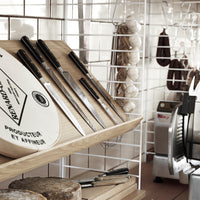 "Stylish black and silver kitchen knives displayed on a wooden rack, surrounded by rustic decor and white shelving."