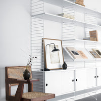 Minimalist white shelving unit with natural wood accents and a monochromatic lamp, featuring a modern geometric pattern.