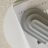 Gray decorative object with wavy pattern resting on a white table, next to a minimalist journal.