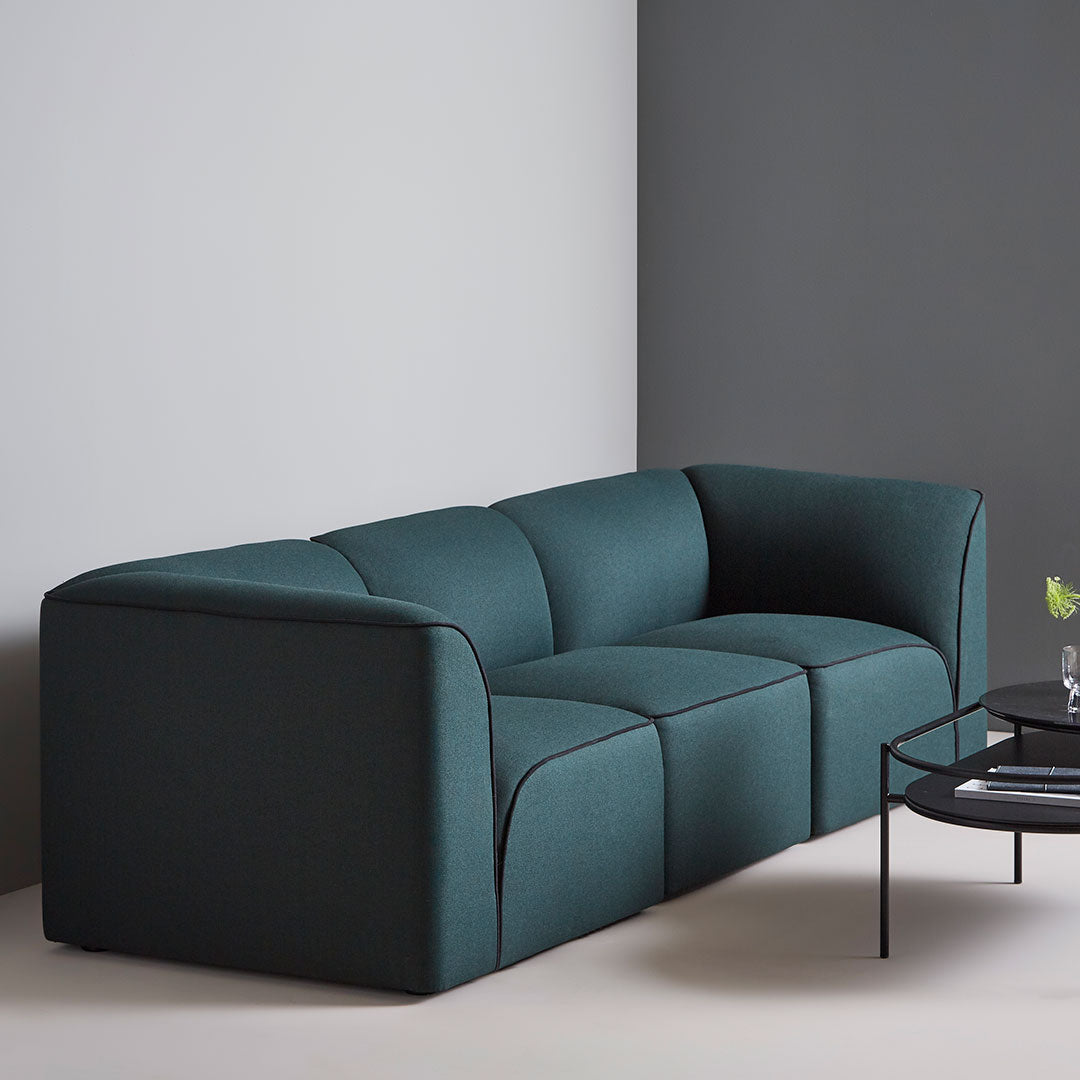 Teal upholstered sofa with sleek lines and a modern design against a minimalist grey backdrop.