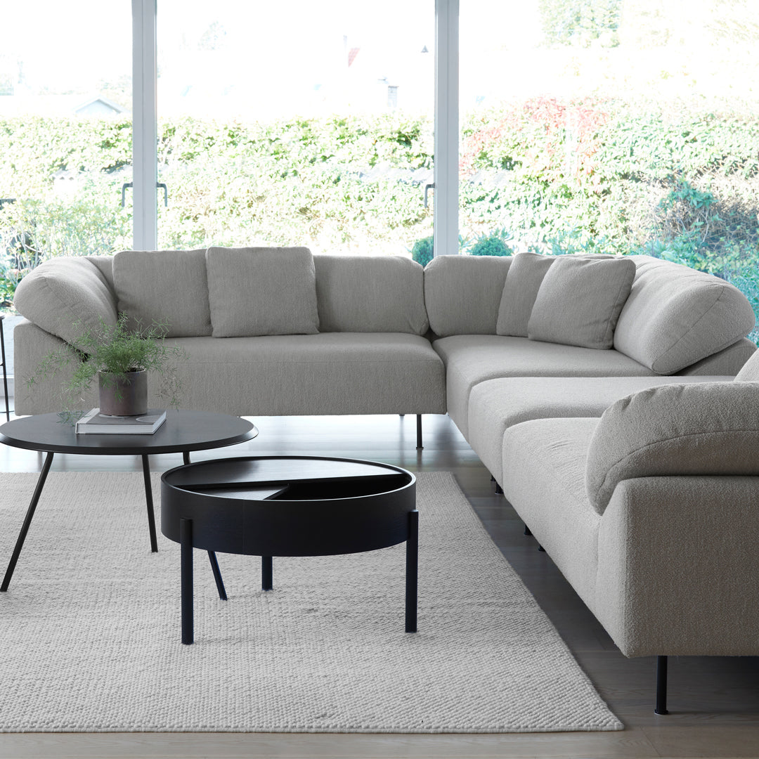 Beige upholstered sectional sofa with soft curves, paired with a sleek black coffee table and light gray area rug.