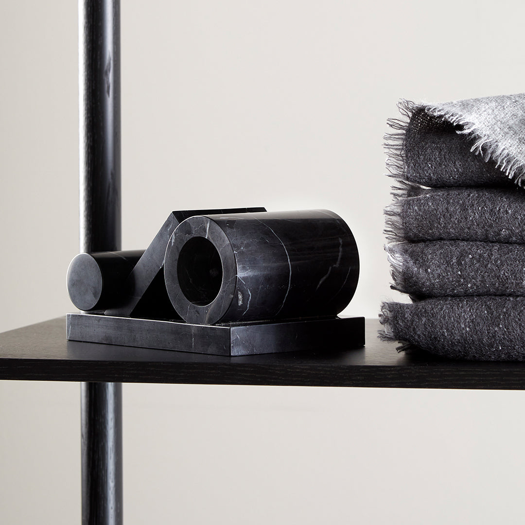 Black geometric sculpture on shelf next to gray fringed blankets, creating a modern and stylish visual contrast.