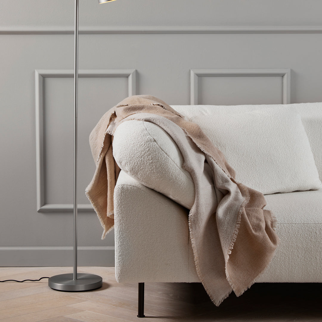Soft beige and taupe throw draped over a white couch, adding warmth and texture to the modern interior.