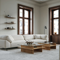 Modern beige sofa with textured upholstery, wooden coffee tables, and neutral gray carpet in a stylish, light-filled room.