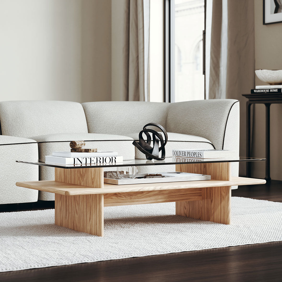 Light wood coffee table with a sleek glass top, set against a neutral rug and soft gray couch. Modern, minimalist design.