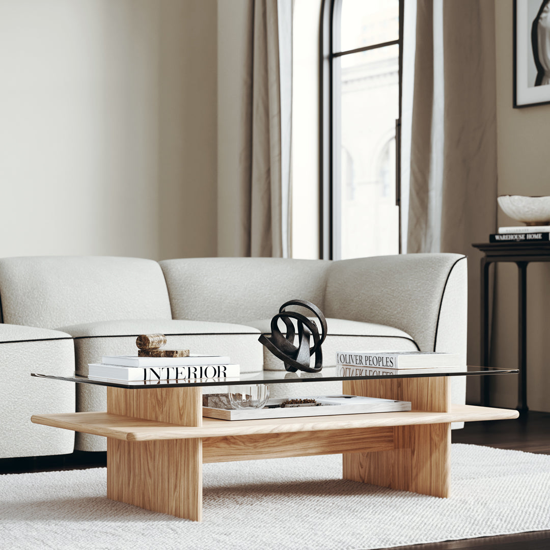 Modern wood coffee table with light oak finish and sleek glass top, complemented by a soft beige rug and minimalist decor.