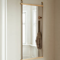 Sleek rectangular mirror with a minimalist gold frame, reflecting warm neutral tones and soft interior lighting.