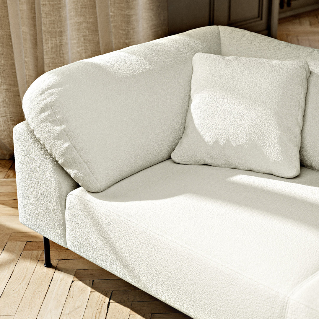 Soft white textured fabric couch with a matching square pillow against a natural wood floor.