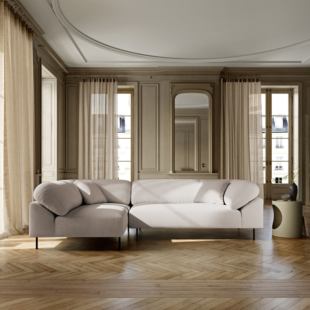 Light beige sectional sofa with soft, rounded cushions set against a neutral-toned room and wooden herringbone flooring.