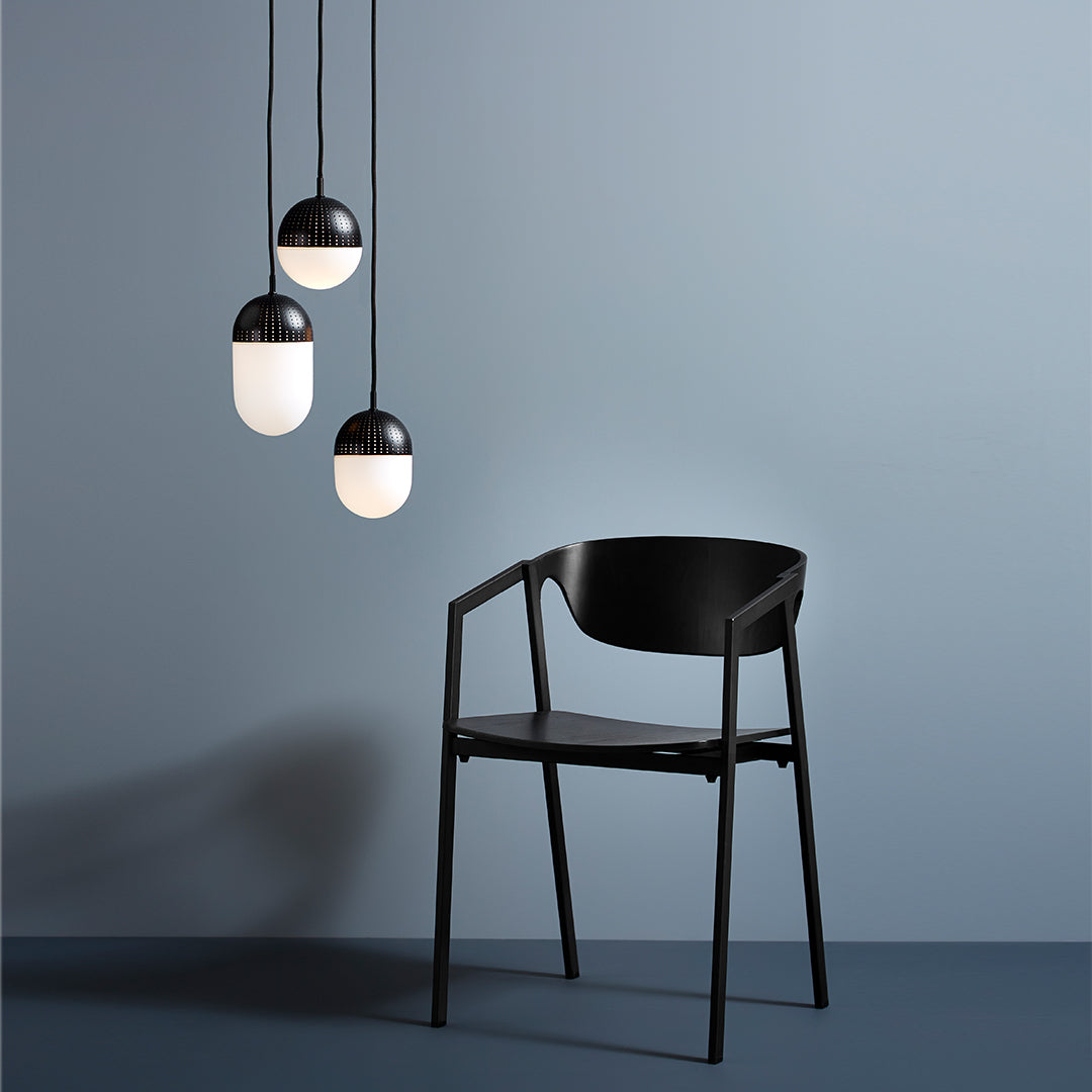 Black chair against a soft blue wall, featuring three rounded black and white pendant lights above.