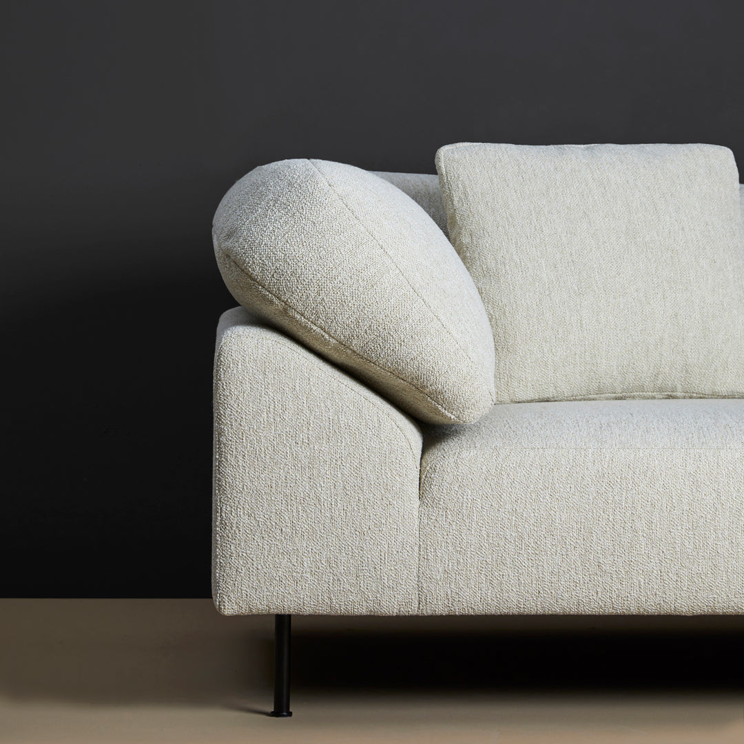 Light gray textured sofa with a round arm cushion against a dark gray backdrop. Modern minimalist design.